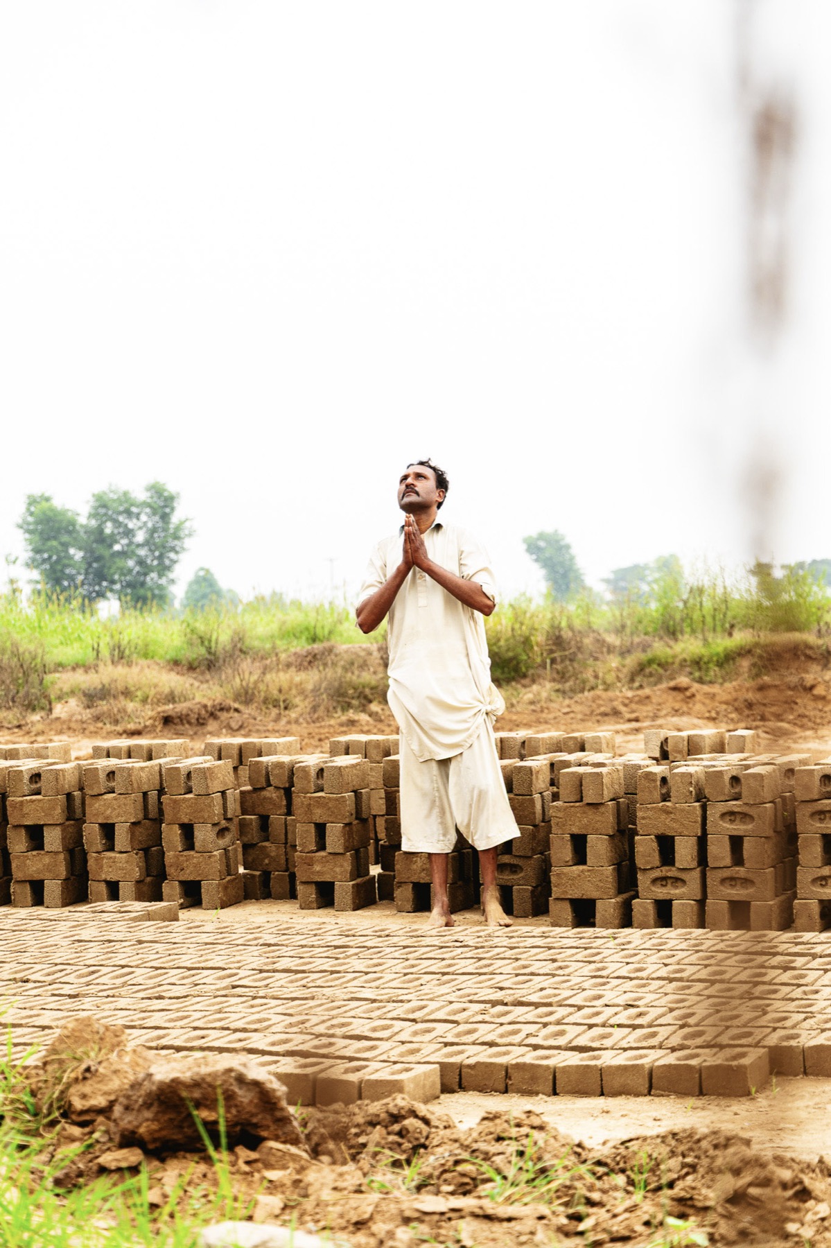 A man prays among rows of drying bricks at a kiln