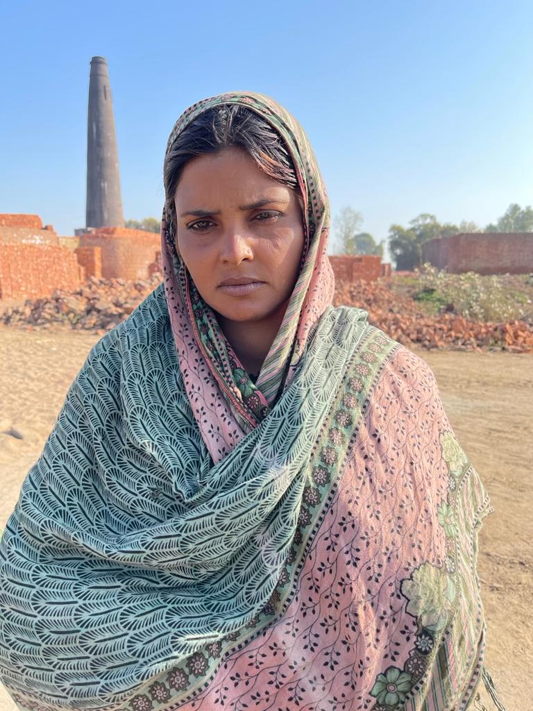 A woman stands before a brick kiln chimney in Pakistan